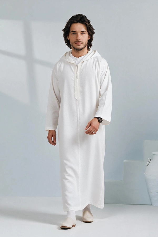 Djellaba blanche à capuche portée par un mannequin masculin barbu marchant sur fond de studio bleu clair